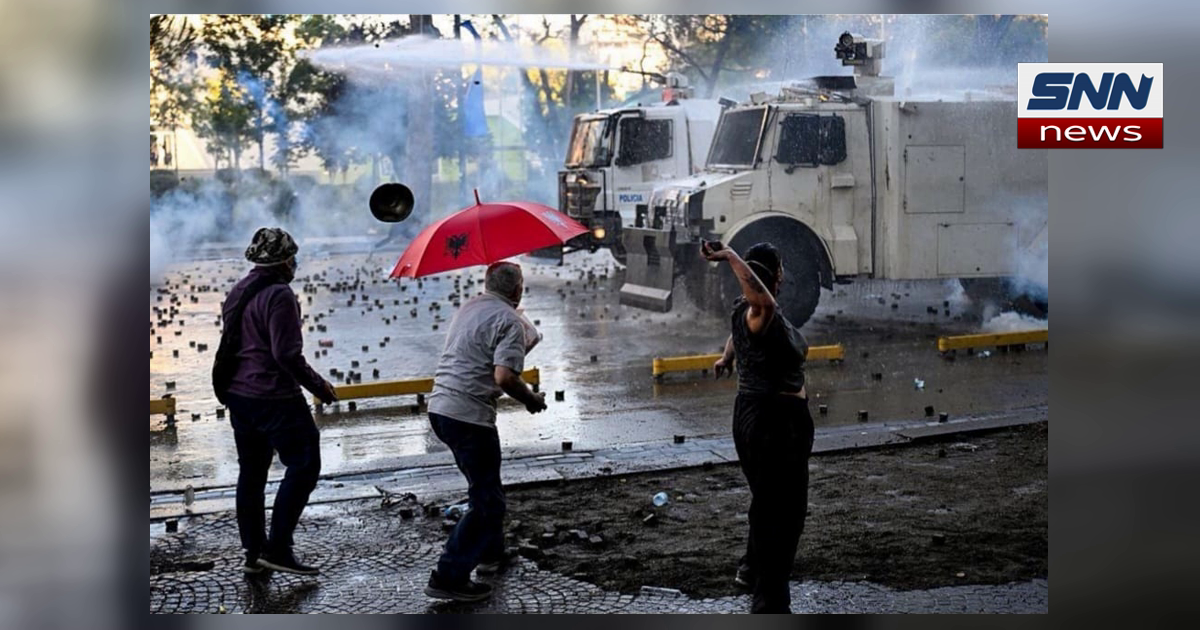 Riot police water cannon spraying protesters in Tirana, Albania, one holding a red umbrella with the Albanian double-headed eagle, SNN News Finland