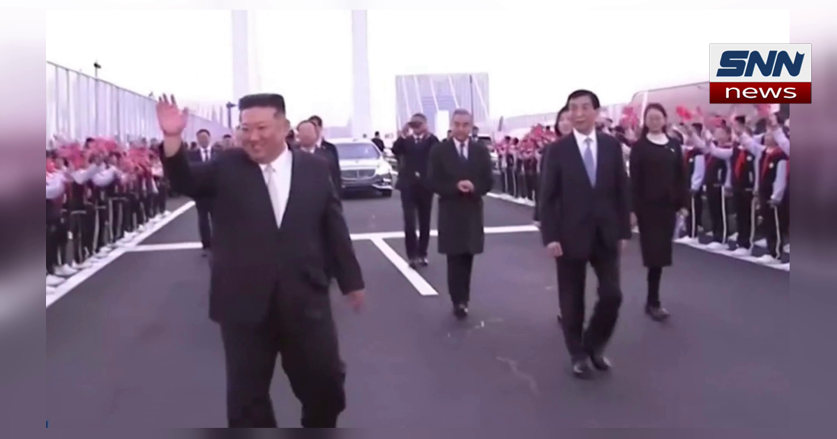 North Korea's Kim Jong Un waving as he walks with Chinese officials past students waving red flags, SNN News Finland