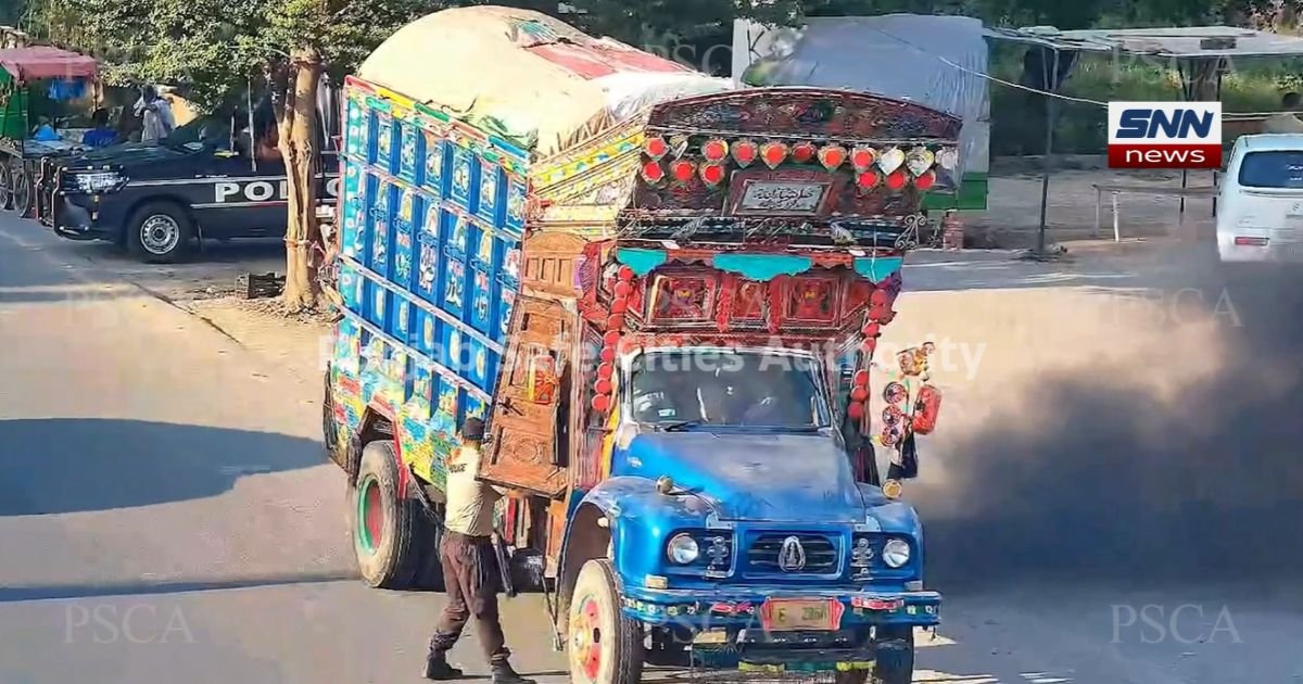 Traffic on a Lahore road with a smoke-emitting vehicle, under a hazy sky"